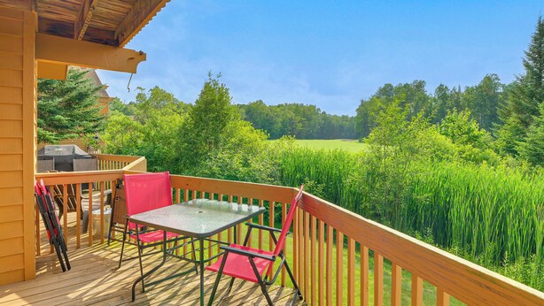 Una terraza de madera con una mesa y sillas, con vista a un campo verde exuberante.
