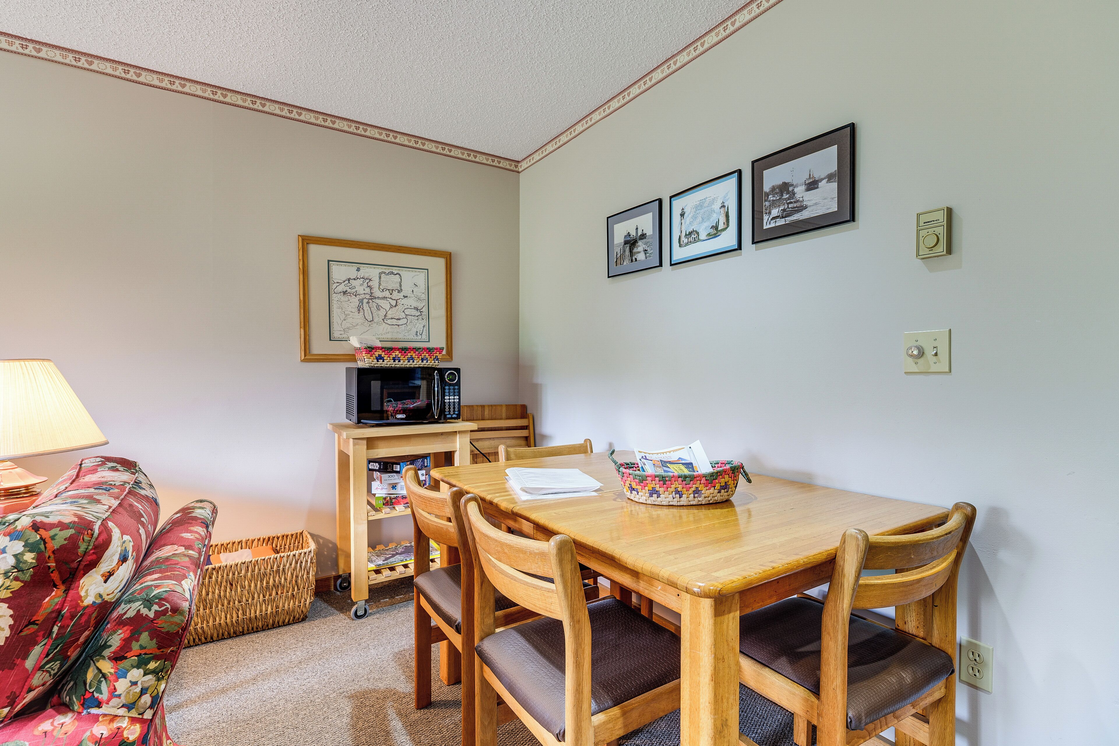 A dining area with a wooden table, chairs, a basket, and a framed map on the wall.