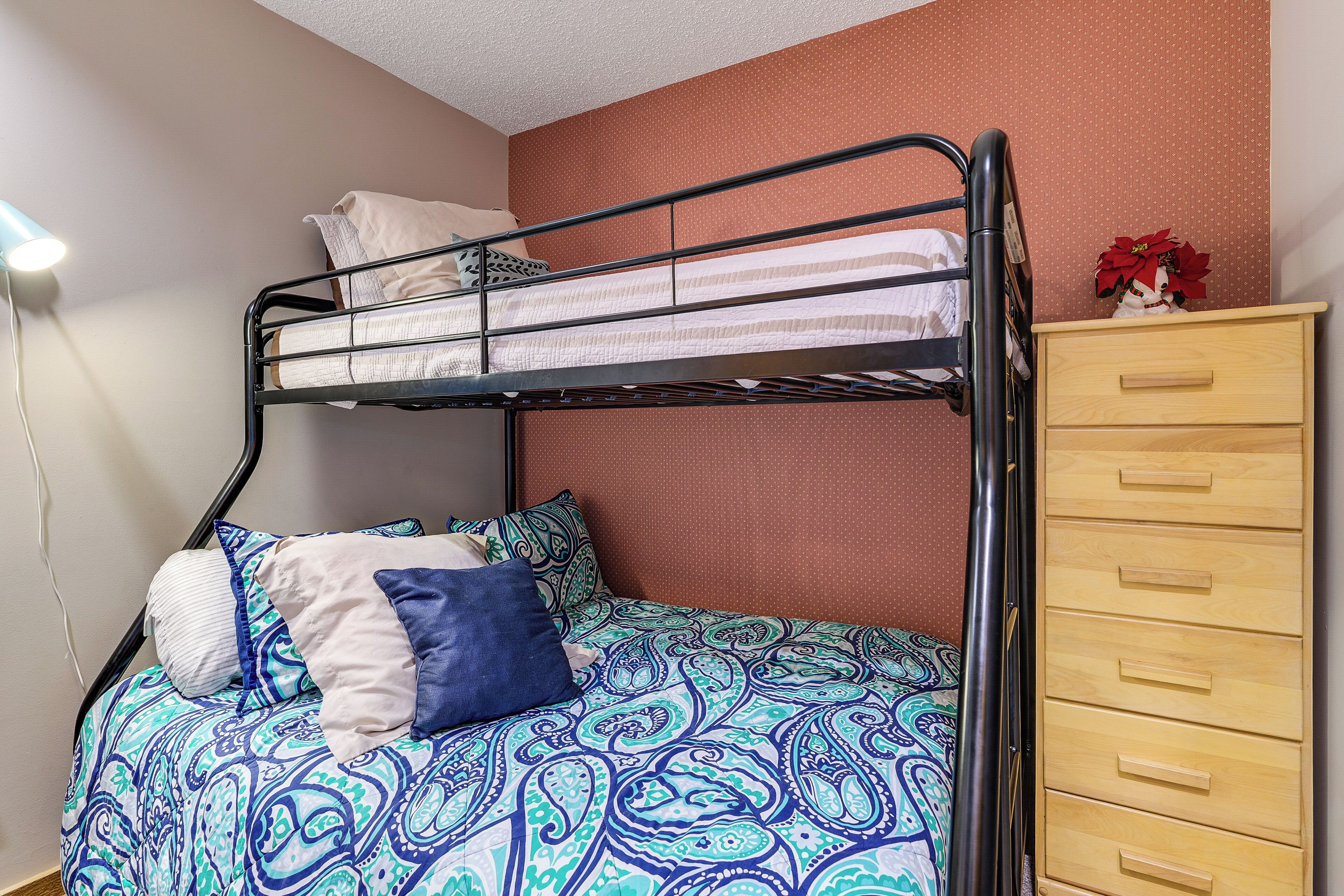 Ein Stockbett mit gemustertem Bettbezug, eine Holzkommode mit Schubladen und eine Wandlampe.