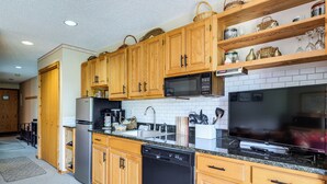 Una cocina con armarios de madera, microondas, lavavajillas, encimera de granito y televisor.