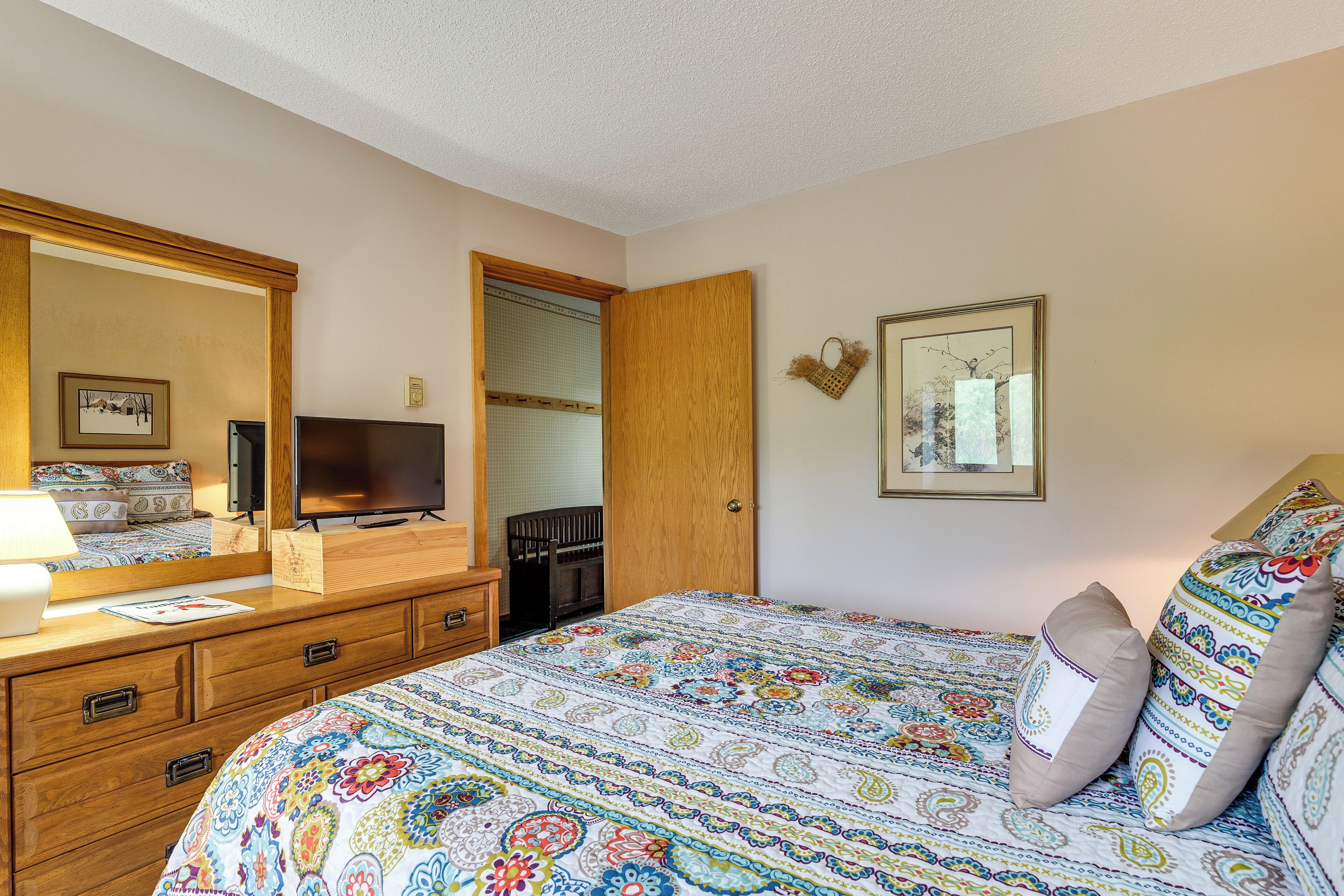 A bedroom with a bed, dresser, television, and a door leading to another room.