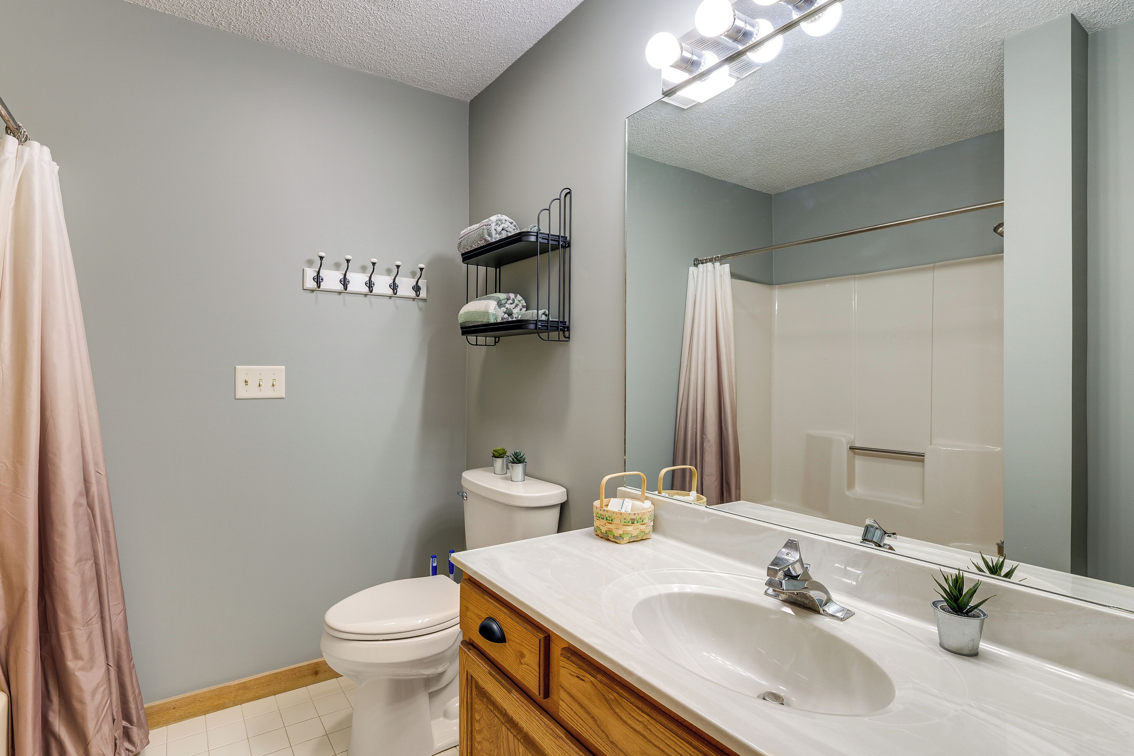 Une salle de bain avec un lavabo blanc, un miroir, un porte-serviettes, des toilettes et un rideau de douche.