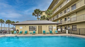 A hotel with a swimming pool, multiple balconies, and palm trees. - Sun-soaked Condo w/ Balcony - Steps to Beach! (Ormond Beach)