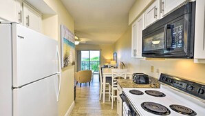 A kitchen with a refrigerator, microwave, stove, and a dining area with chairs and a table. - Sun-soaked Condo w/ Balcony - Steps to Beach! (Ormond Beach)