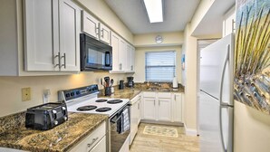 A kitchen with white cabinets, a black microwave, a stove, a refrigerator, and granite countertops. - Sun-soaked Condo w/ Balcony - Steps to Beach! (Ormond Beach)