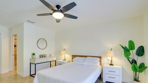 Quarto com cama, mesas de cabeceira, escrivaninha, ventoinha no teto e um vaso de planta.
