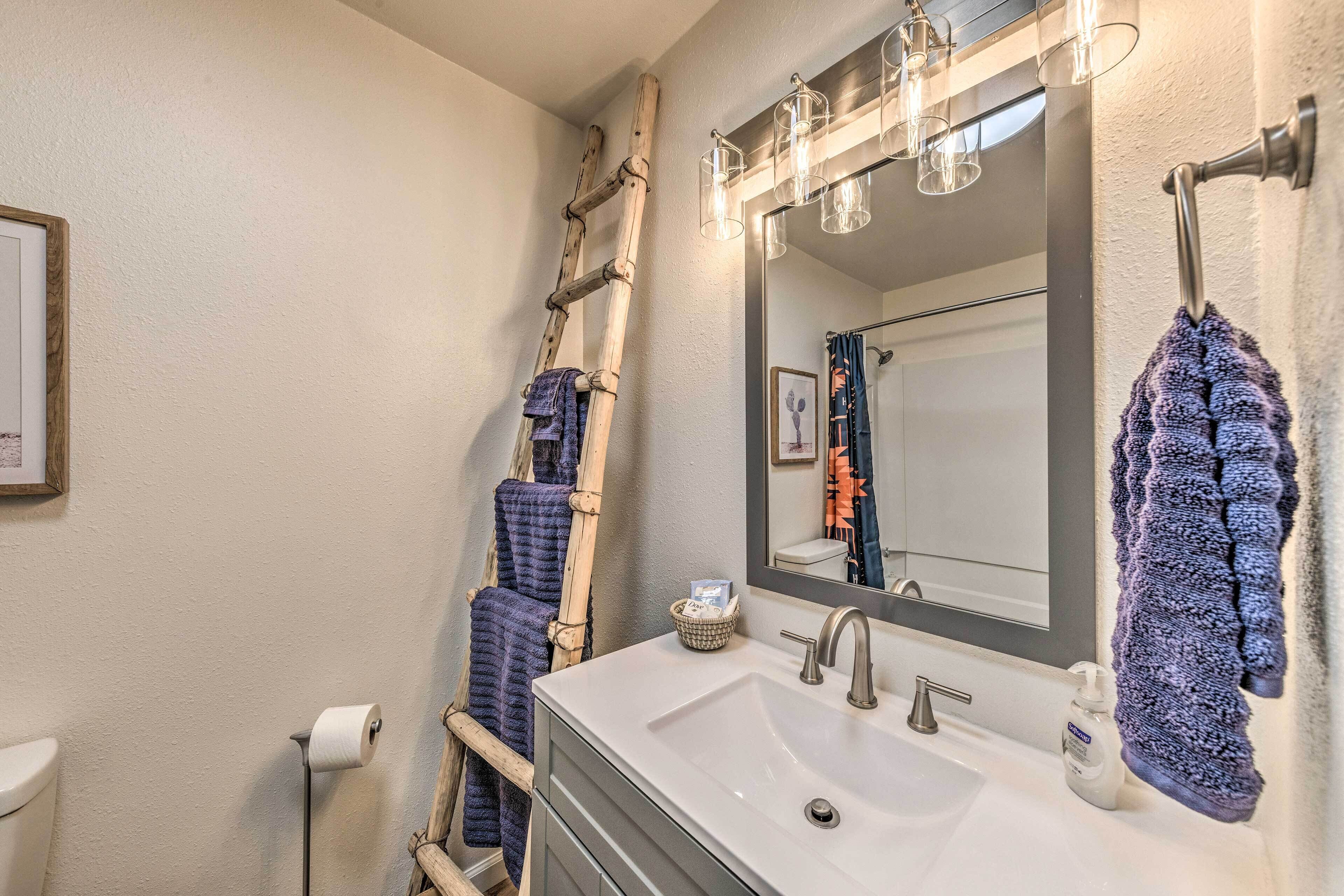 A bathroom with a white sink, a mirror with lights, a wooden ladder, and towels.