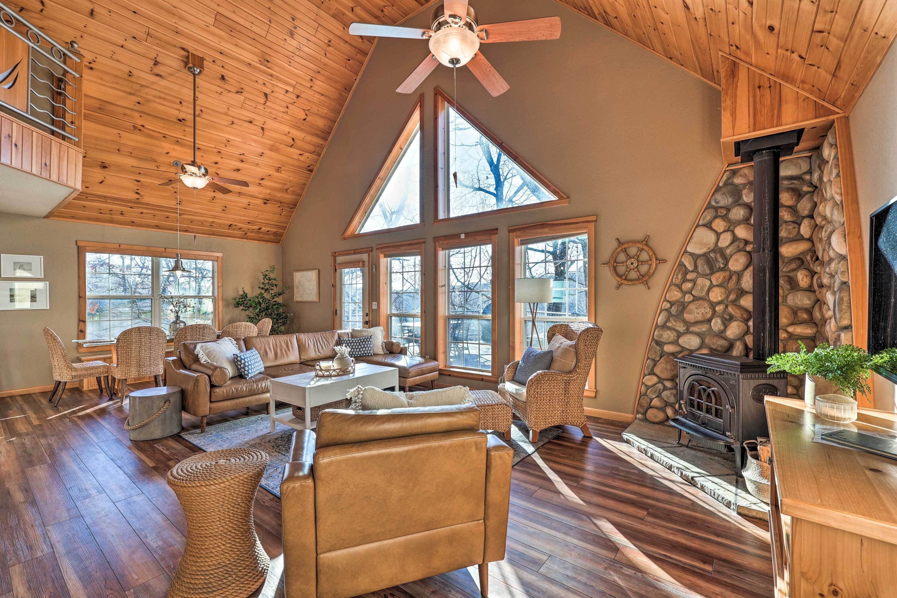 A spacious living room with high ceilings, large windows, a stone fireplace, and a cozy seating area with wicker furniture.