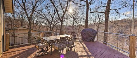 A wooden deck with a table and chairs, surrounded by trees and a view of the landscape.