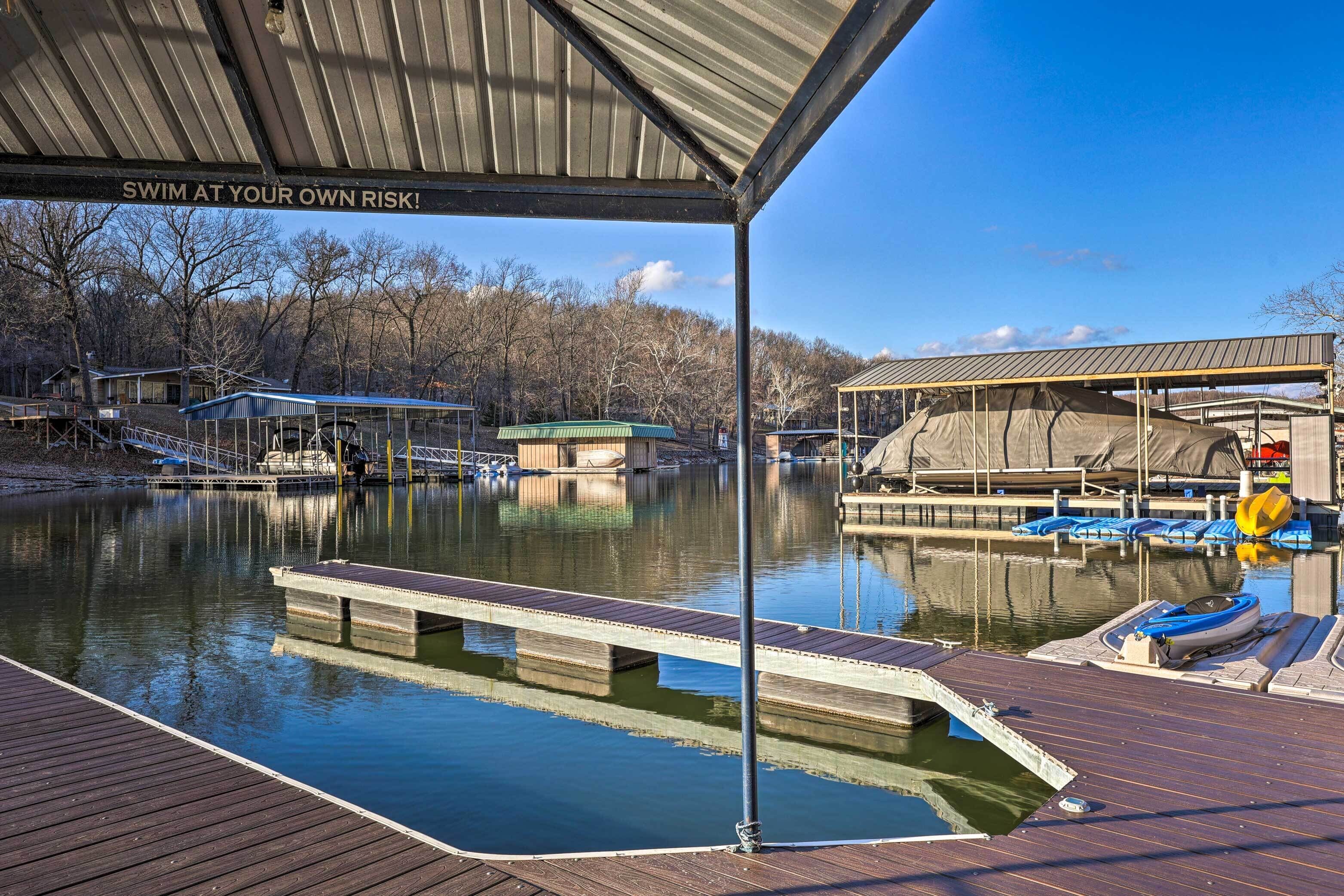 A dock with boats, a covered area with a warning sign, and a calm water body surrounded by trees.