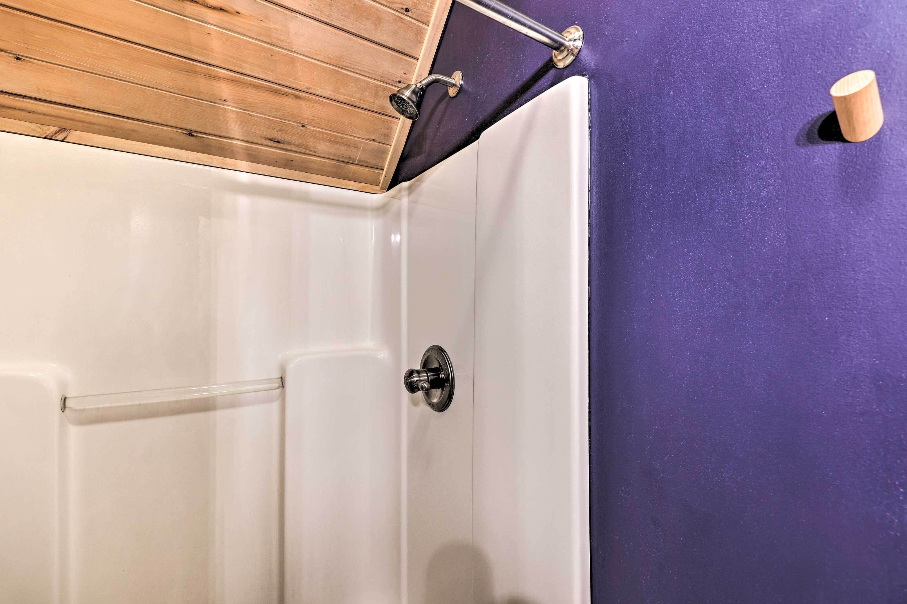 Un baño con ducha, techo de madera y pared morada.