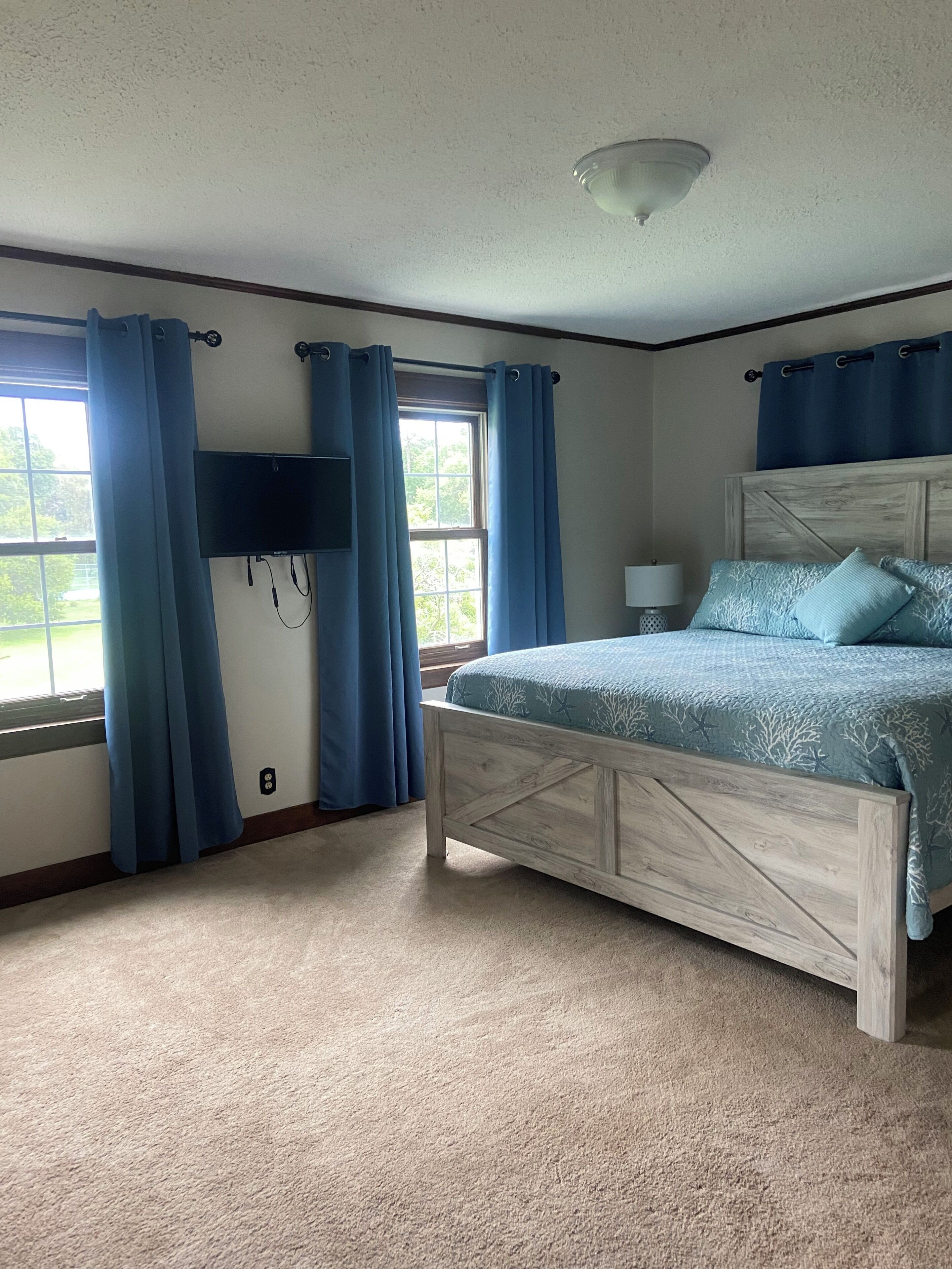 A bedroom with a bed, a TV mounted on the wall, and a window with curtains.