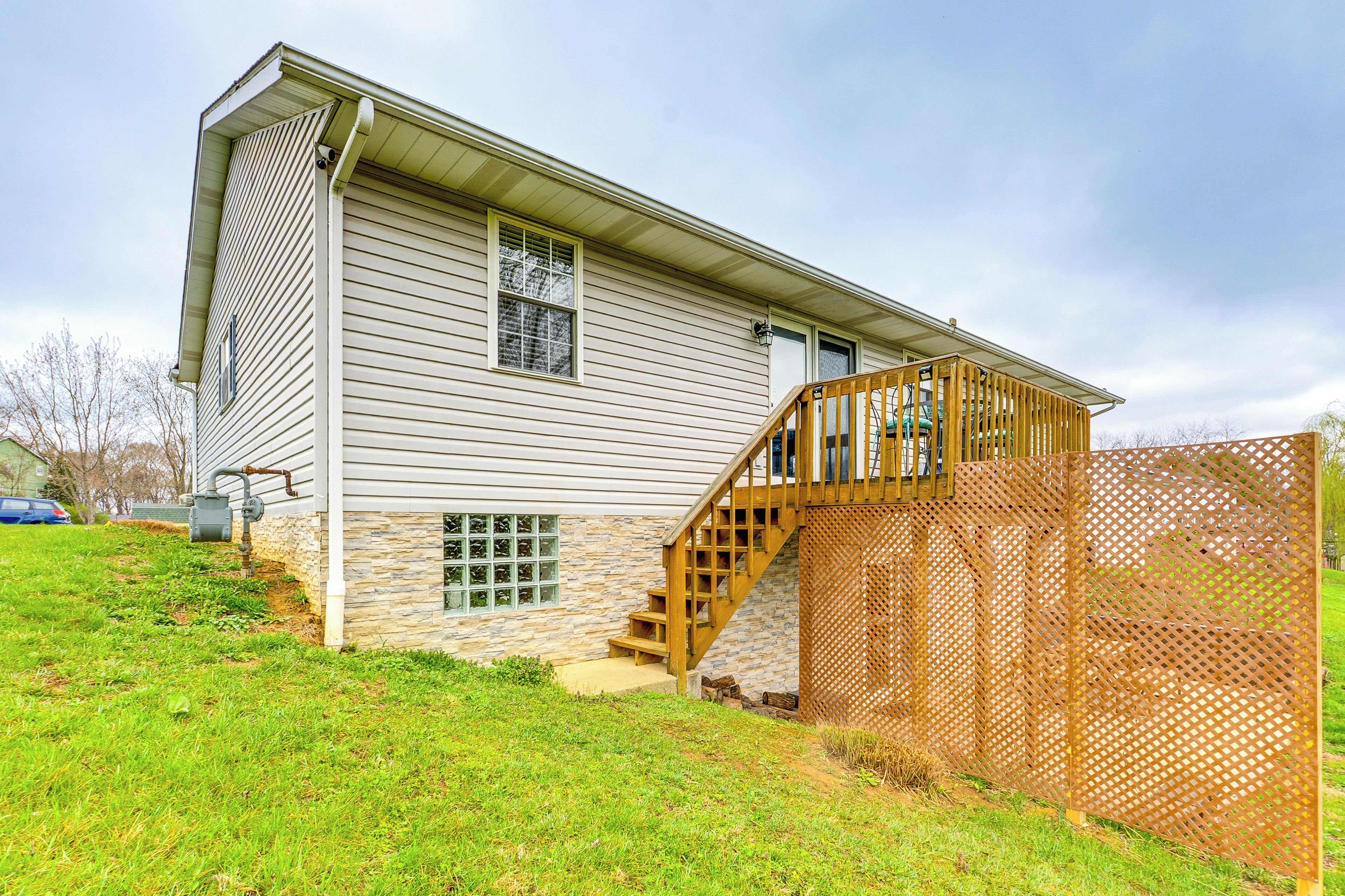 A two-story house with a stone foundation, a wooden deck, and a staircase leading to the second floor.