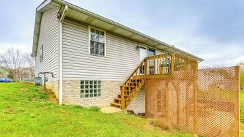 A two-story house with a stone foundation, a wooden deck, and a staircase leading to the second floor.