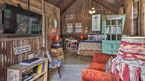 A rustic room with a wooden ceiling, a bed, a desk with a computer, and a television.