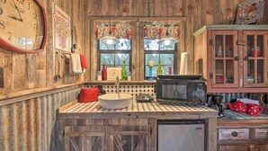 A rustic kitchen with a vintage clock, a sink, a microwave, and wooden cabinets.