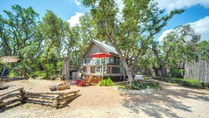 A rustic cabin with a large deck, surrounded by trees and a gravel driveway.