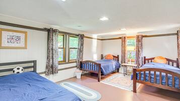 A room with three beds, a small table, and a window with curtains.