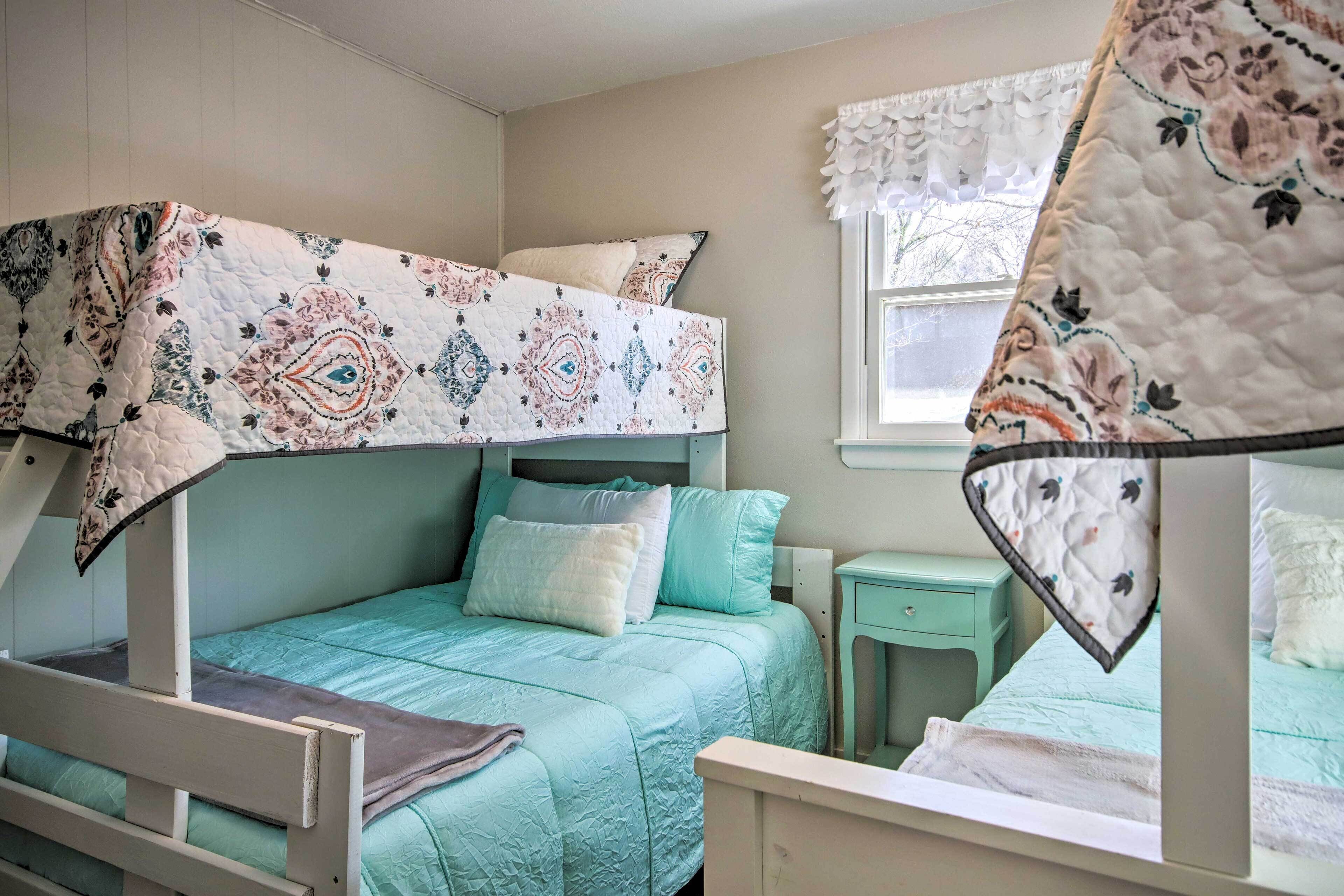 A bunk bed with a patterned quilt, a small bedside table, and a window with a decorative valance.