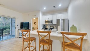 A modern kitchen with white cabinets, stainless steel appliances, and a large window overlooking a garden. - Sunset Beach Retreat - Monthly Rentals Welcome! (Sunset Beach)