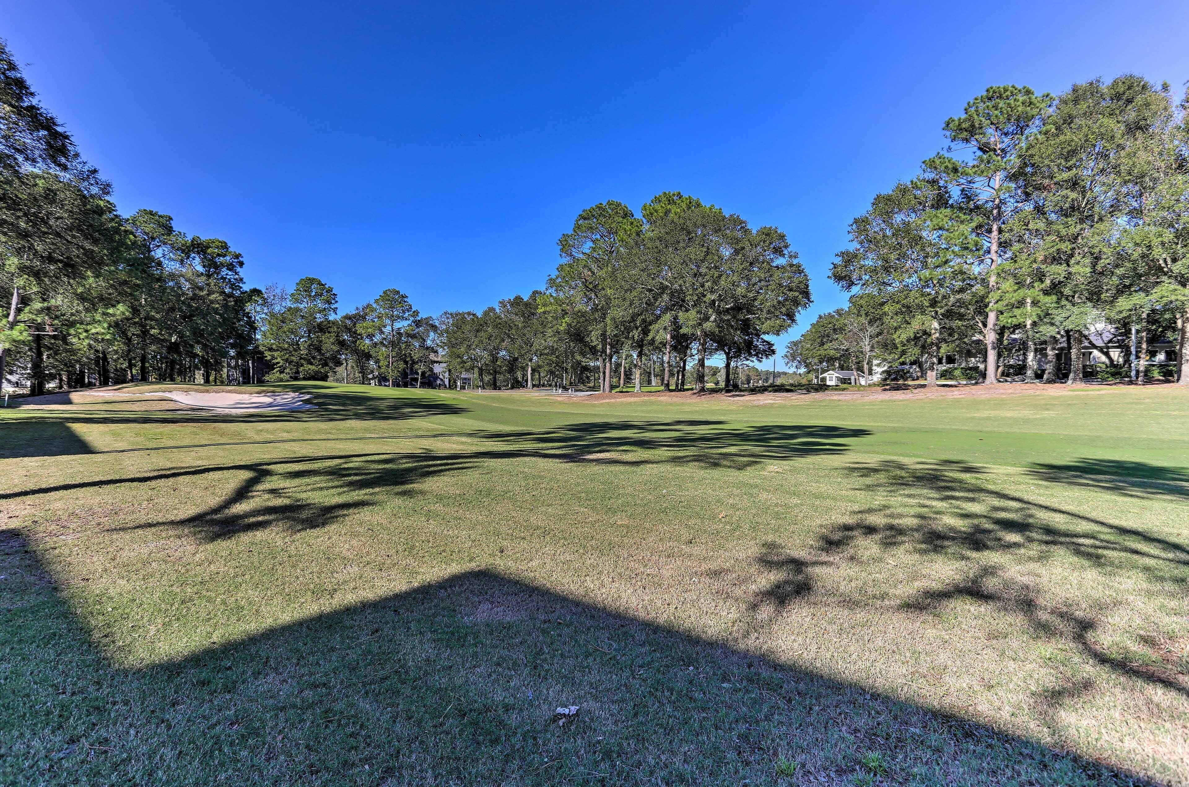 A golf course with a clear sky, well-maintained grass, and tall trees.