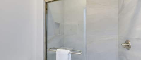 A modern bathroom with a glass shower enclosure, a white toilet, and a towel rack.
