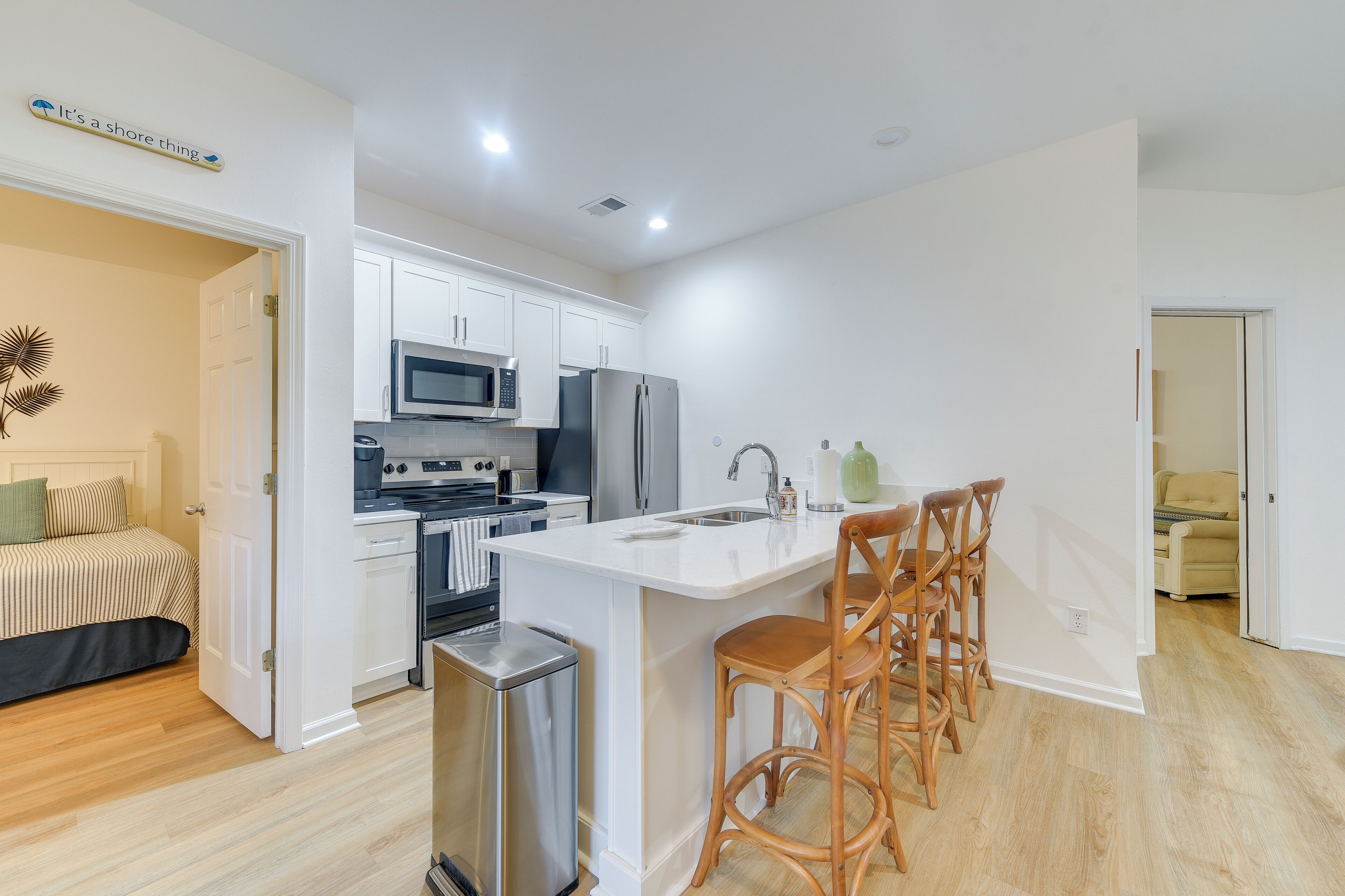 A modern kitchen with white cabinetry, stainless steel appliances, and a bar area with wooden stools.