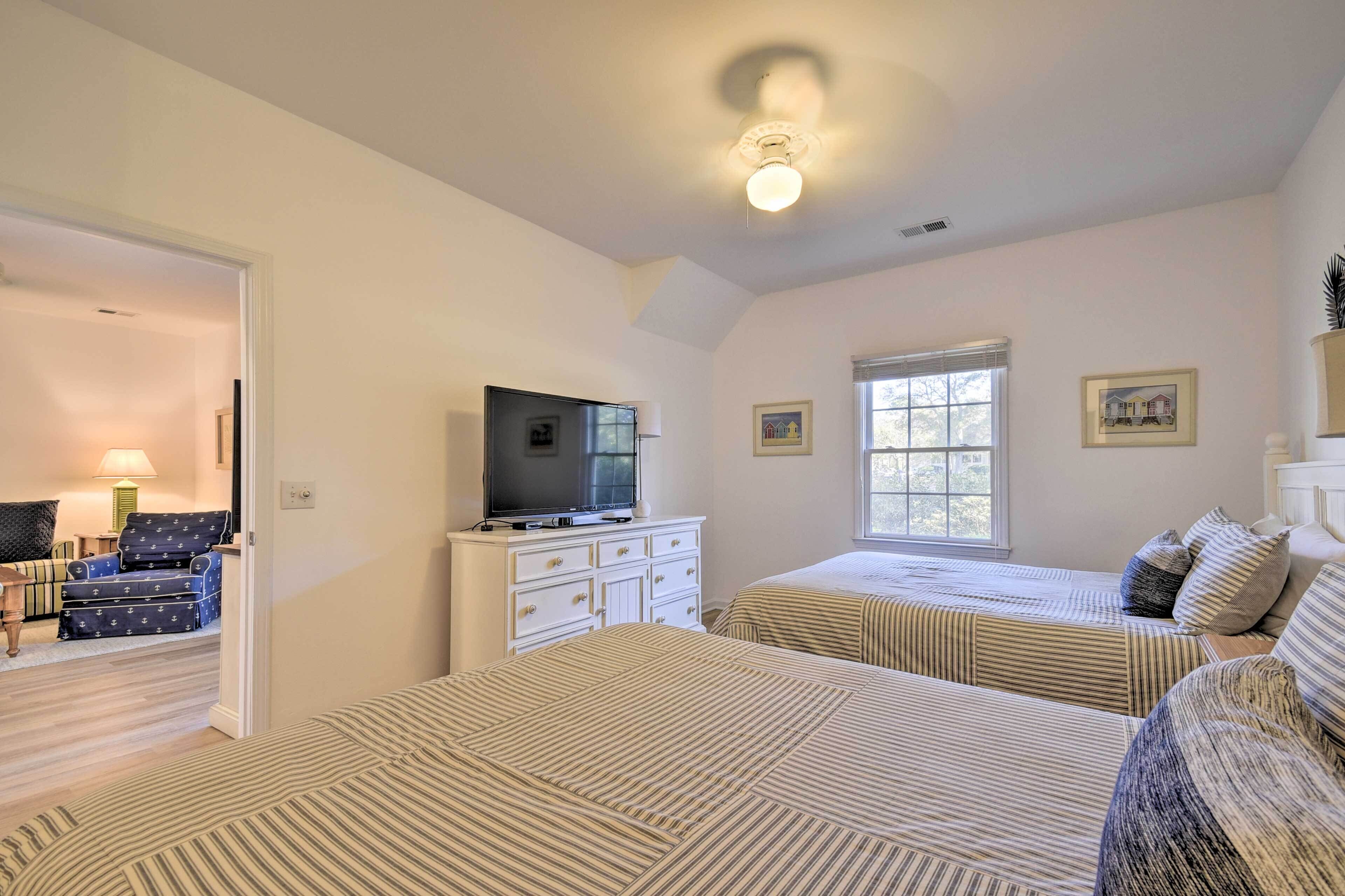 A hotel room with two beds, a television on a dresser, and a window with blinds.
