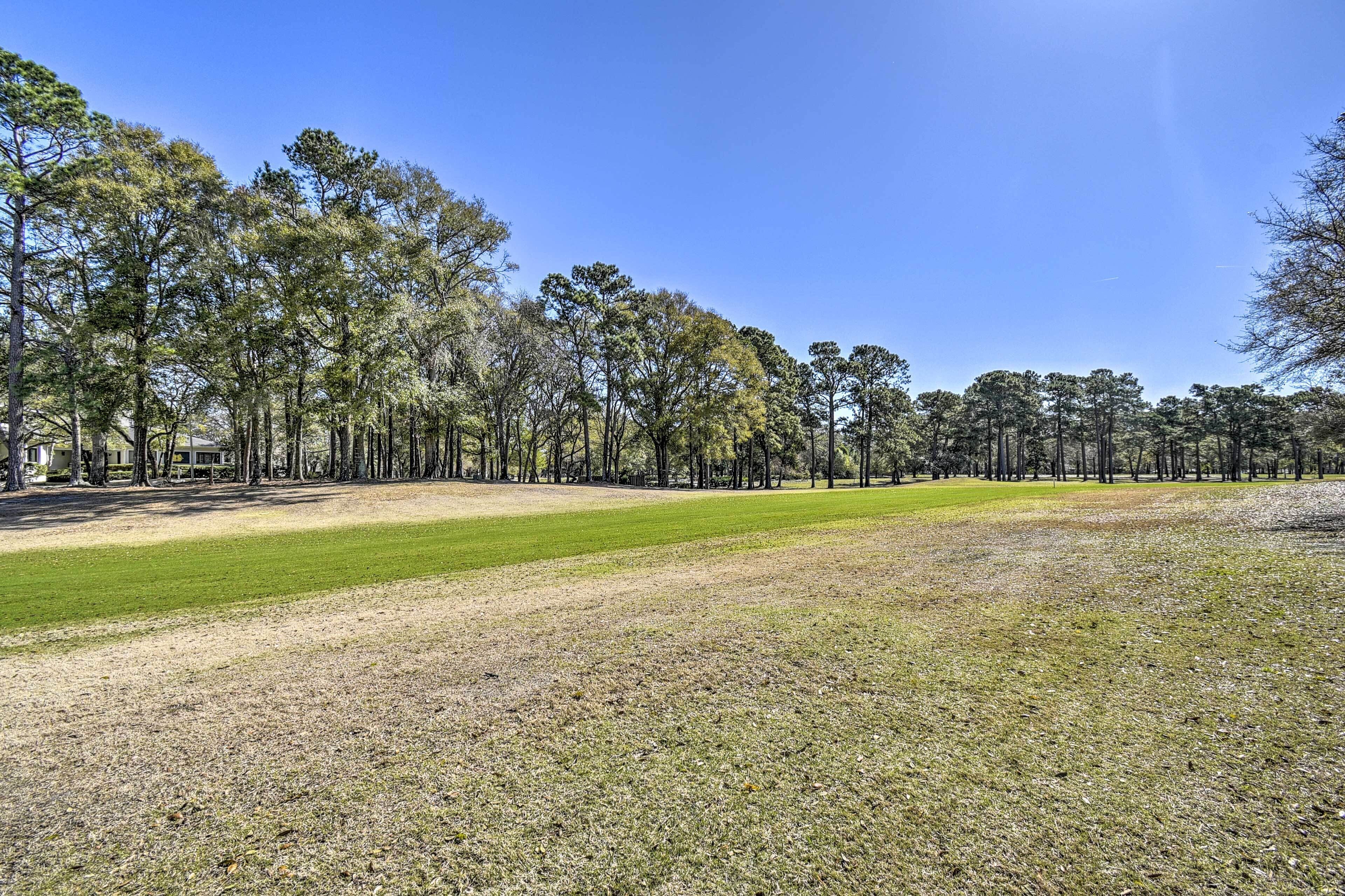 Un terrain de golf avec un ciel dégagé, de l’herbe verte et une rangée d’arbres.
