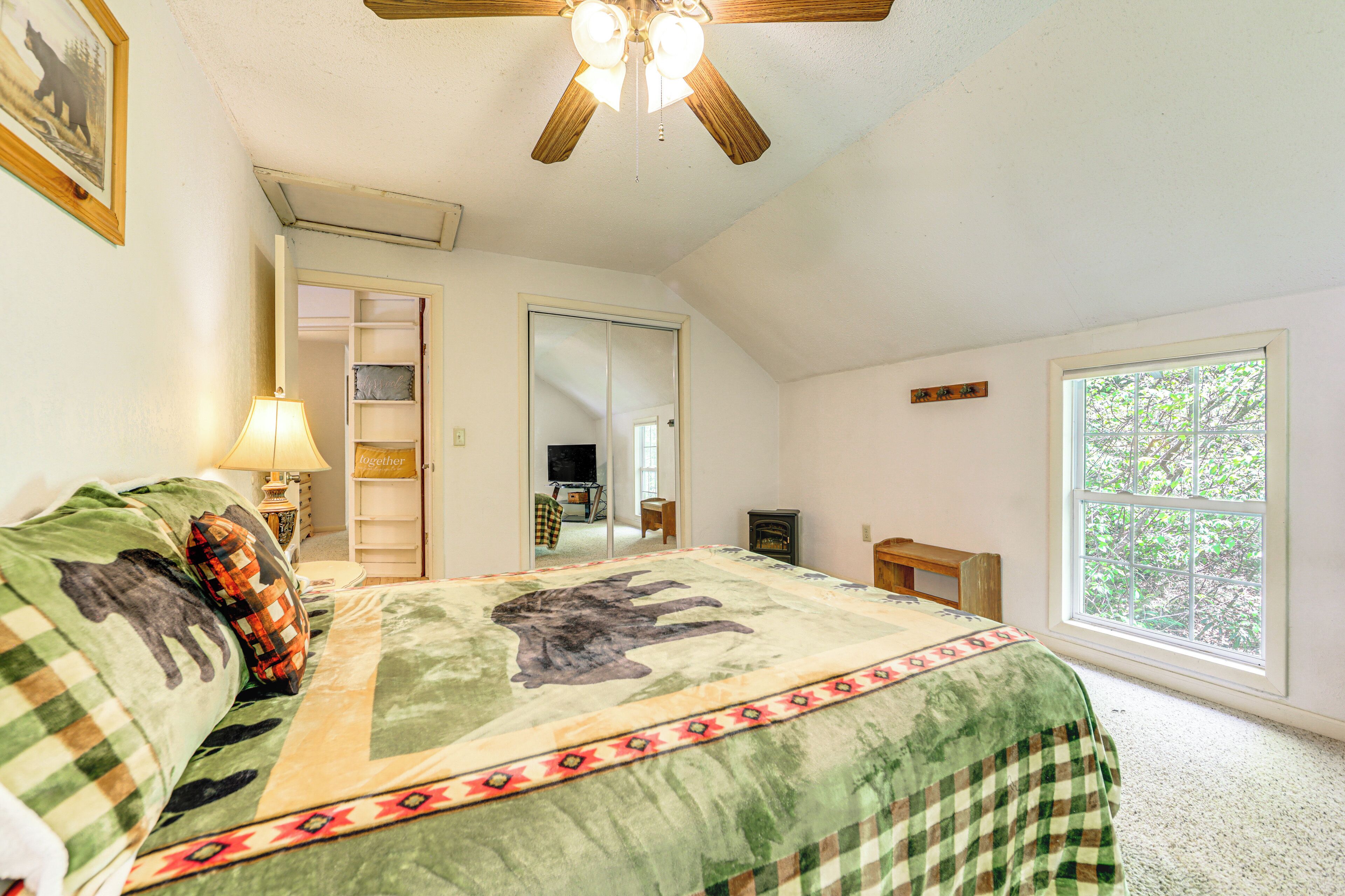 Une chambre à coucher comprenant un lit, un ventilateur de plafond, une fenêtre et une porte donnant sur une salle de bain.