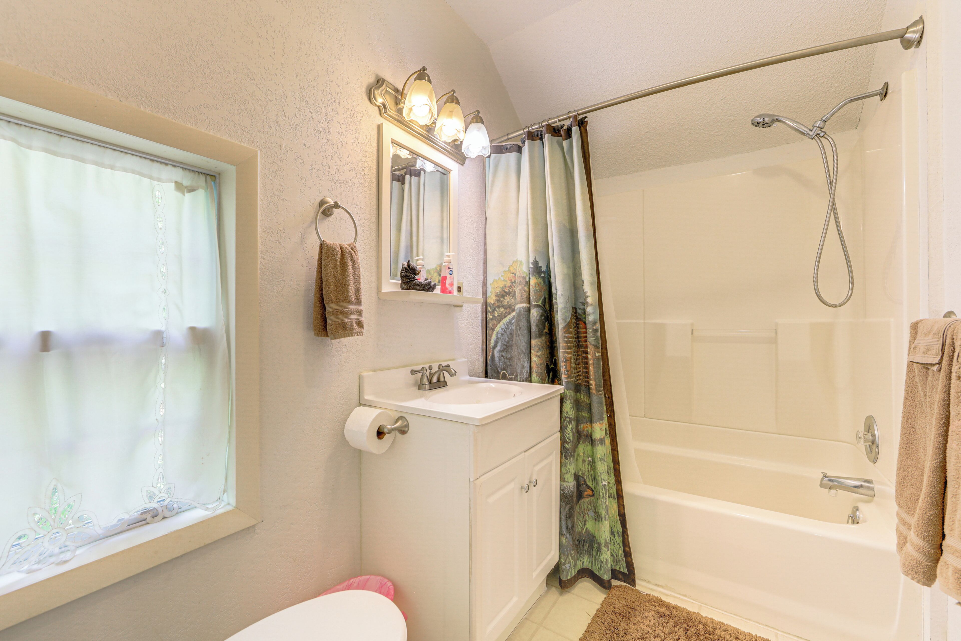 A bathroom with a toilet, sink, mirror, shower, and window.