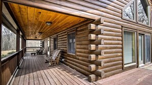 Une cabane en rondins dotée d’une terrasse en bois, de grandes fenêtres et d’un porche abrité.