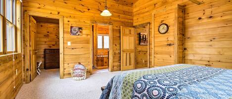 A wooden cabin bedroom with a bed, a clock, and a door leading to a bathroom.
