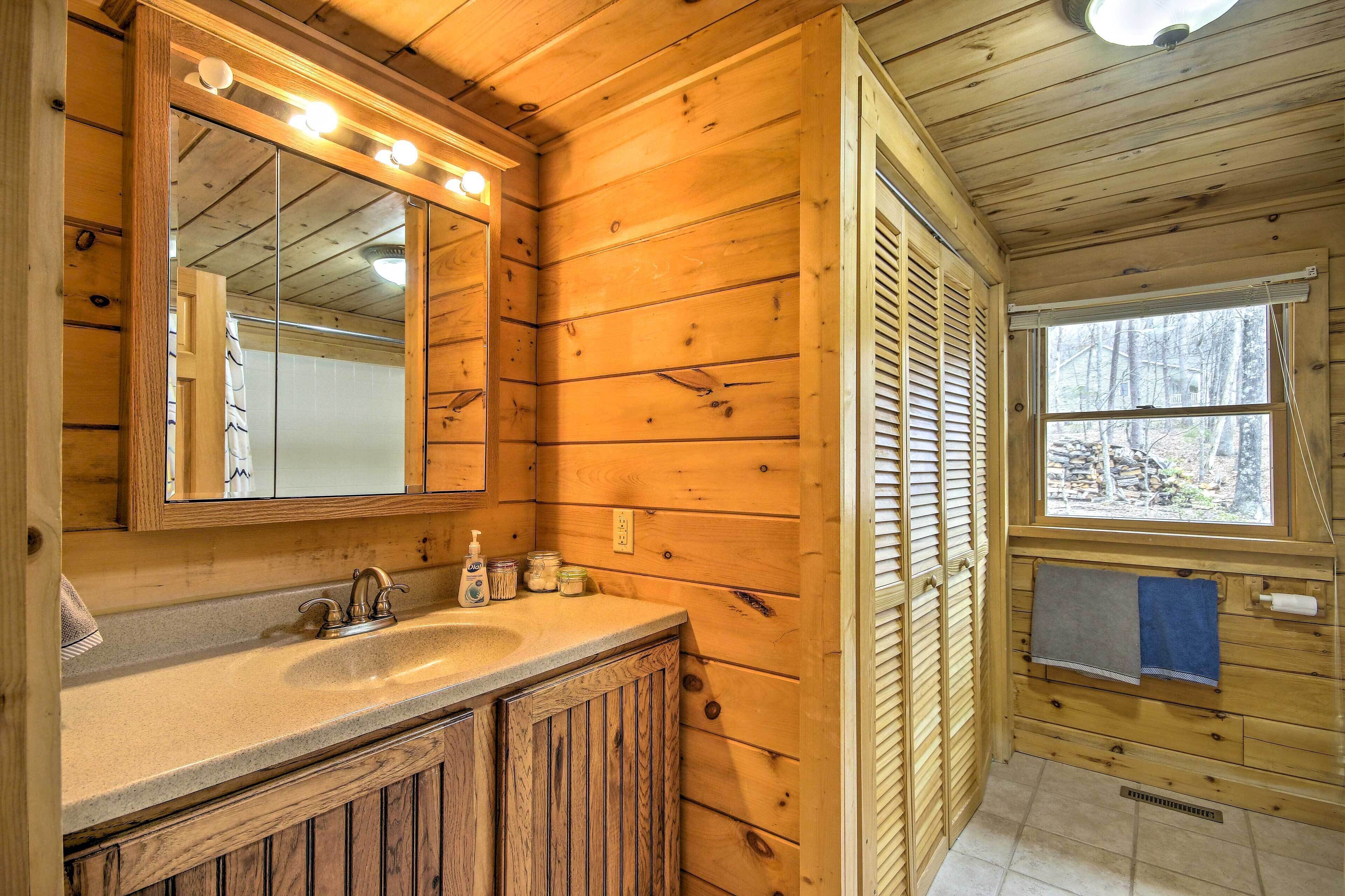 A wooden cabin bathroom with a large mirror, sink, and window.