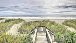 Een houten looppad dat naar een strand leidt, onder een bewolkte lucht.