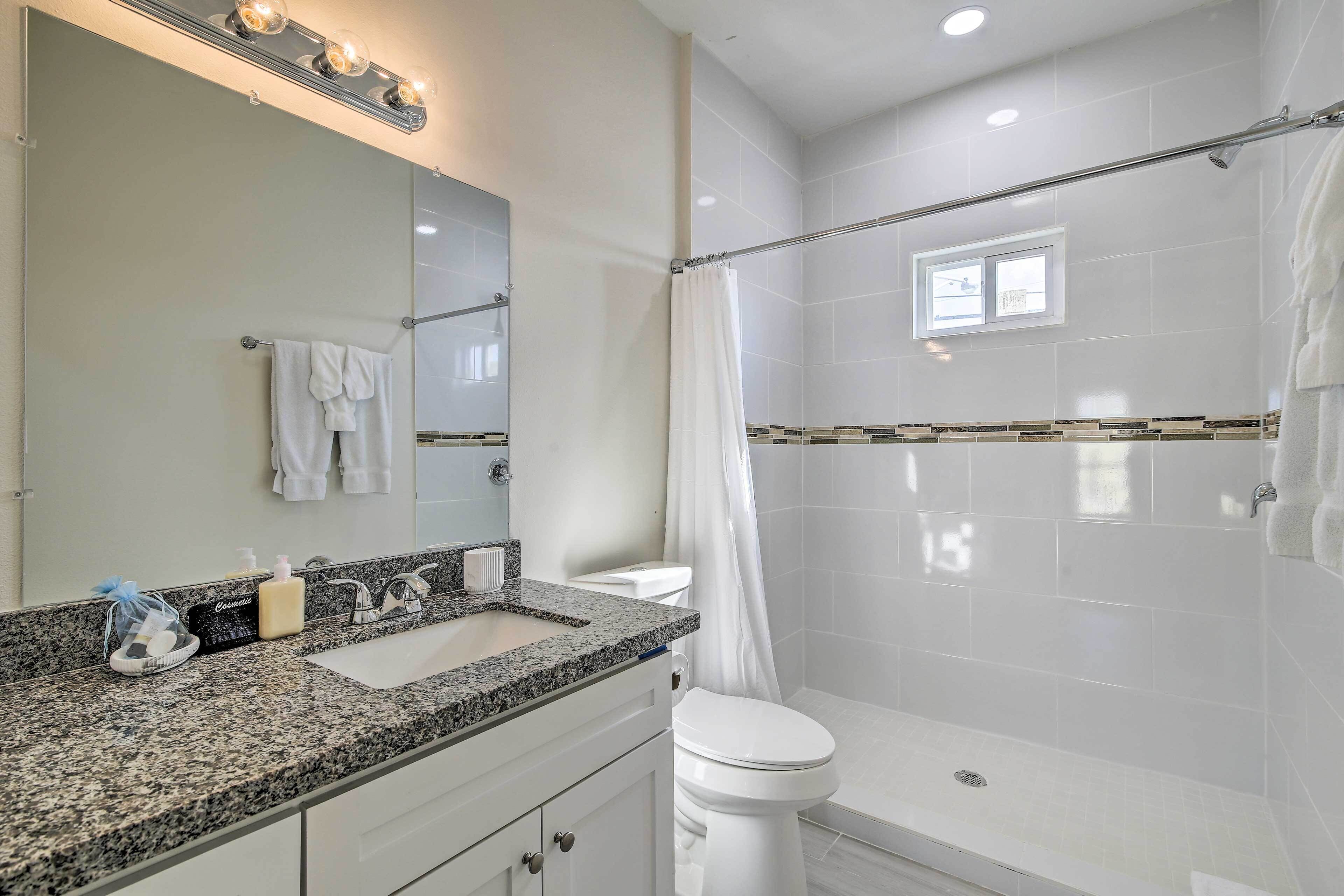 A bathroom with a granite countertop, white sink, and a shower area.