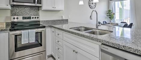 A modern kitchen with granite countertops, stainless steel appliances, white cabinetry, and pendant lighting.