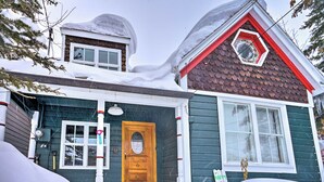 Uma casa de dois andares com porta de madeira, um pequeno alpendre e telhado coberto de neve.