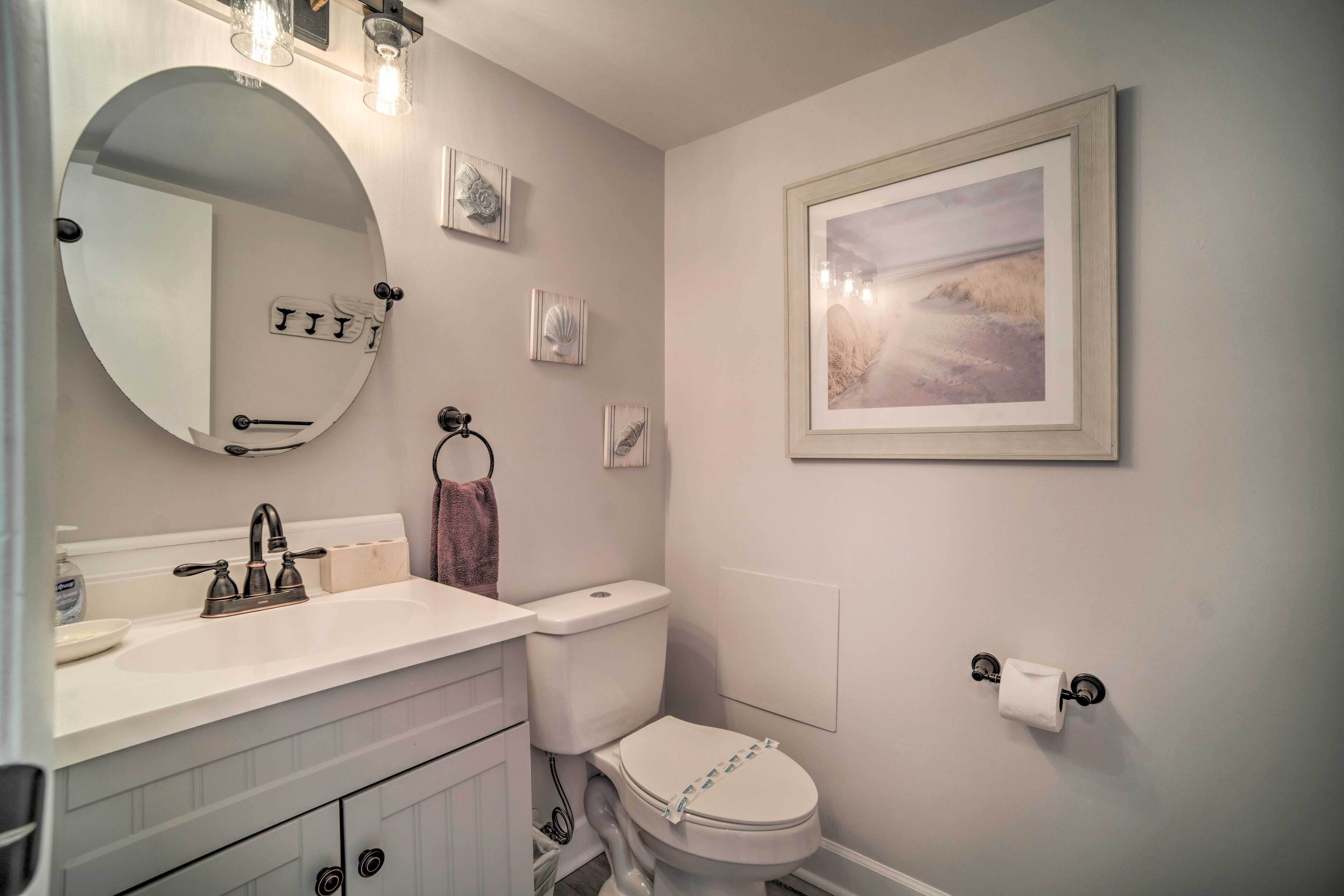 A bathroom with a round mirror, a toilet, a sink, and a framed picture on the wall.
