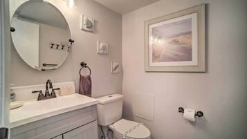 A bathroom with a round mirror, a toilet, a sink, and a framed picture on the wall.