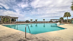 Una piscina con una pérgola y palmeras al fondo.