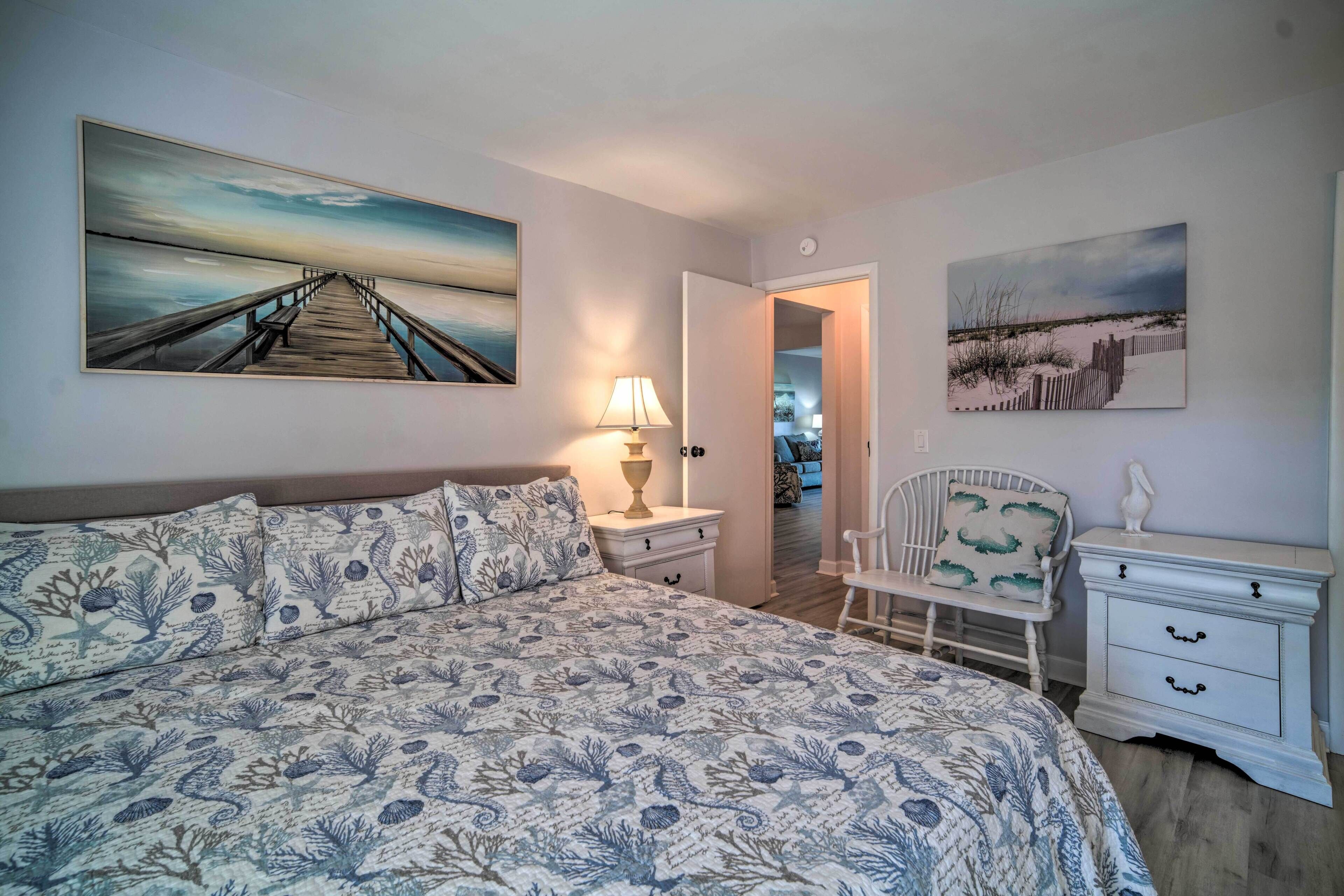 A bedroom with a large bed, a nightstand, a chair, and two paintings on the wall.