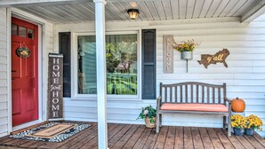 A porch with a red door, a welcome sign, a bench, and potted plants. - Cedar Falls Country Cottage Near the Zoo! (Randleman)