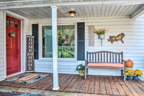 A porch with a red door, a welcome sign, a bench, and potted plants. - Cedar Falls Country Cottage Near the Zoo! (Randleman)