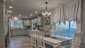 A spacious kitchen with light green cabinets, a white dining table with plaid tablecloth, and a chandelier. - Cedar Falls Country Cottage Near the Zoo! (Randleman)