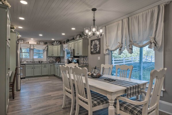 A spacious kitchen with light green cabinets, a white dining table with plaid tablecloth, and a chandelier. - Cedar Falls Country Cottage Near the Zoo! (Randleman)