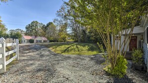 A gravel driveway leading to a white picket fence and a house with a red roof. - Cedar Falls Country Cottage Near the Zoo! (Randleman)