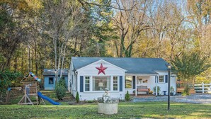 A white house with a red star on the front, a porch, and a play area with a slide. - Cedar Falls Country Cottage Near the Zoo! (Randleman)