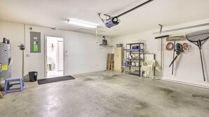 A spacious garage with a concrete floor, a ceiling-mounted projector, a broom, a mop, and a shelf with cleaning supplies. - Ocala Gem: 5 Mi to World Equestrian Center! (Ocala)