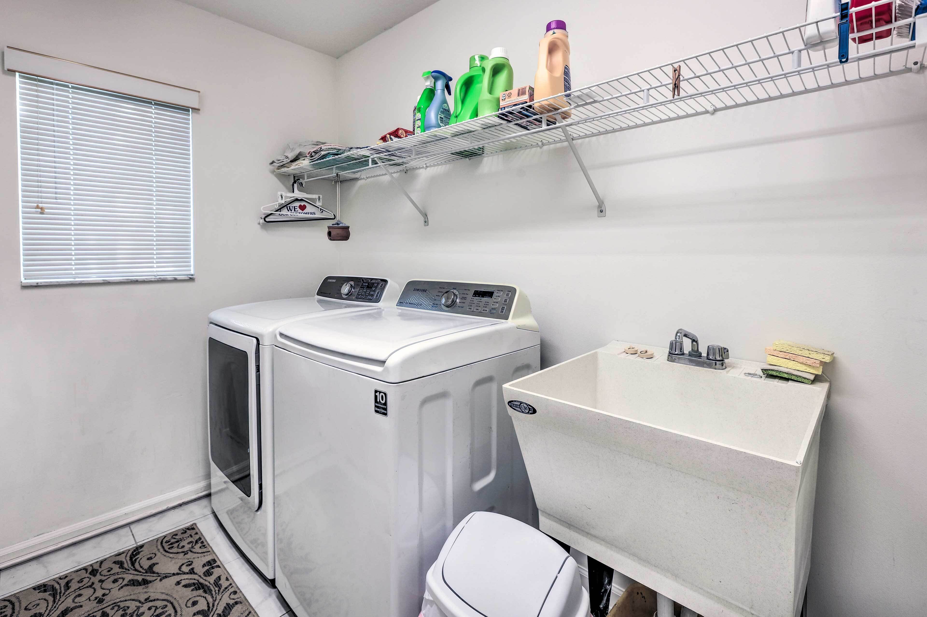 A laundry room with two washing machines, a sink, and a shelf with cleaning supplies.
